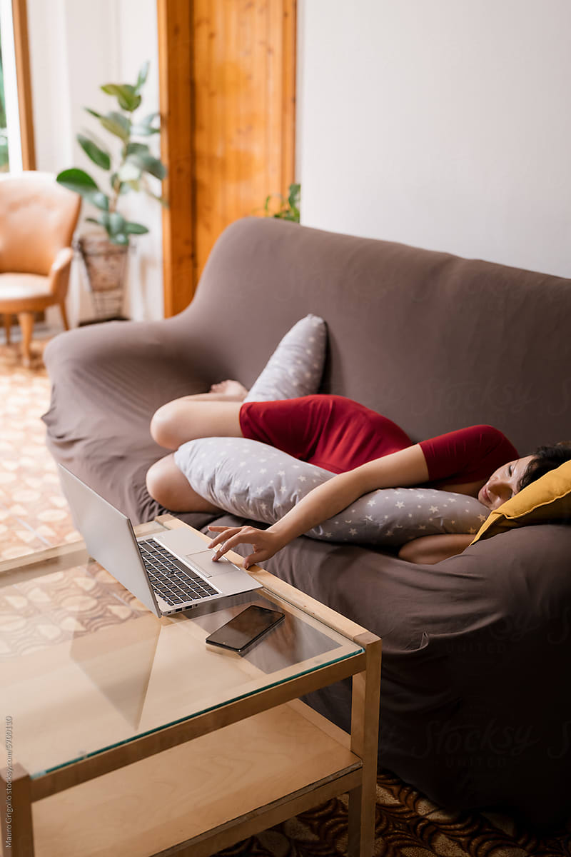Pregnant woman lying on the sofa and using a laptop