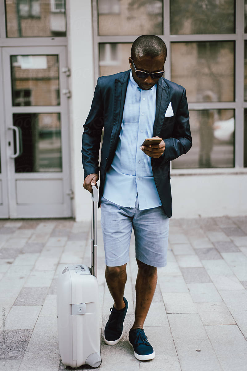 Black man with suitcase using smartphone