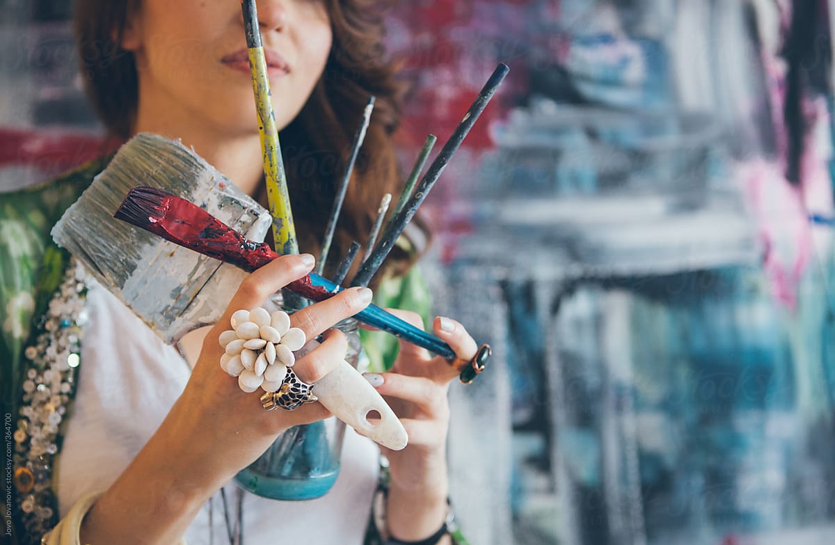 Young artist holding messy paint brushes in a studio