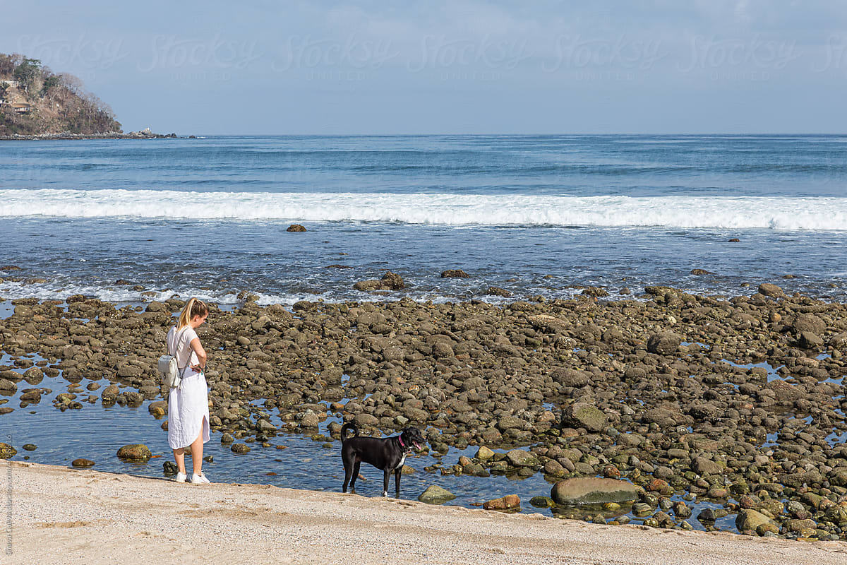 Woman in white clothes with her dog in front of a beach