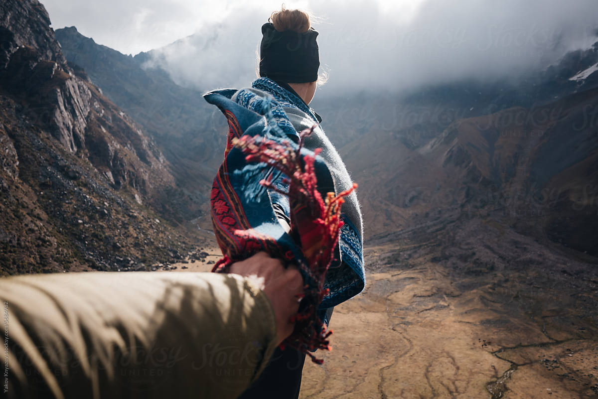 Woman in poncho holding hand of partner in mountains