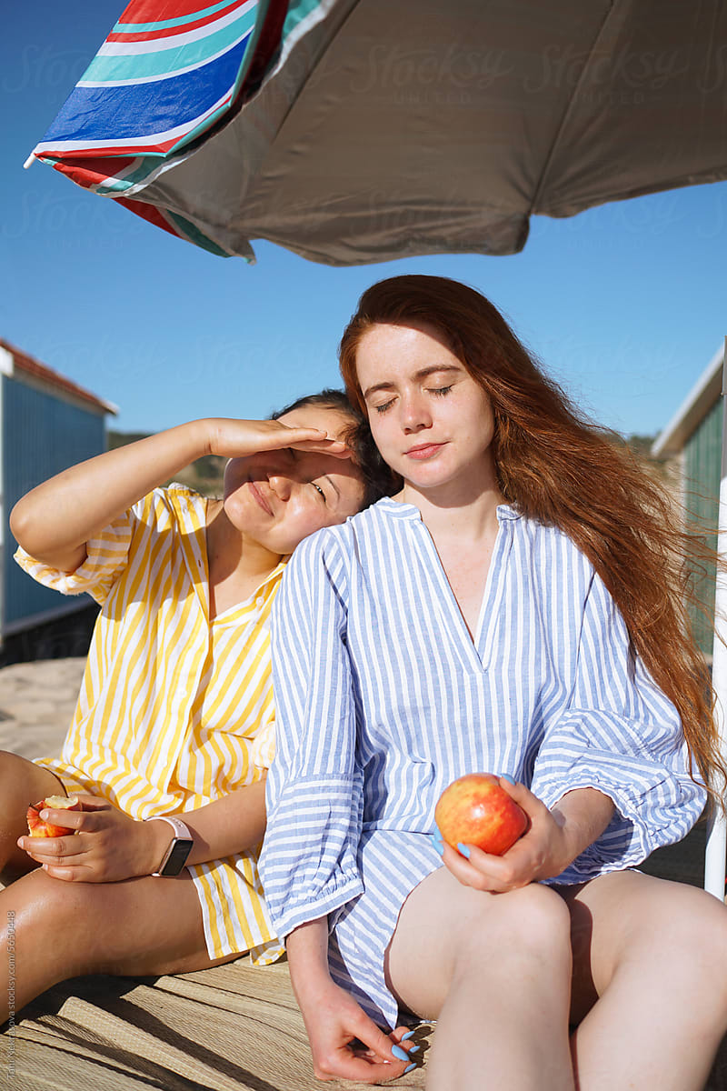 Two girls sitting on the beach and eating apples