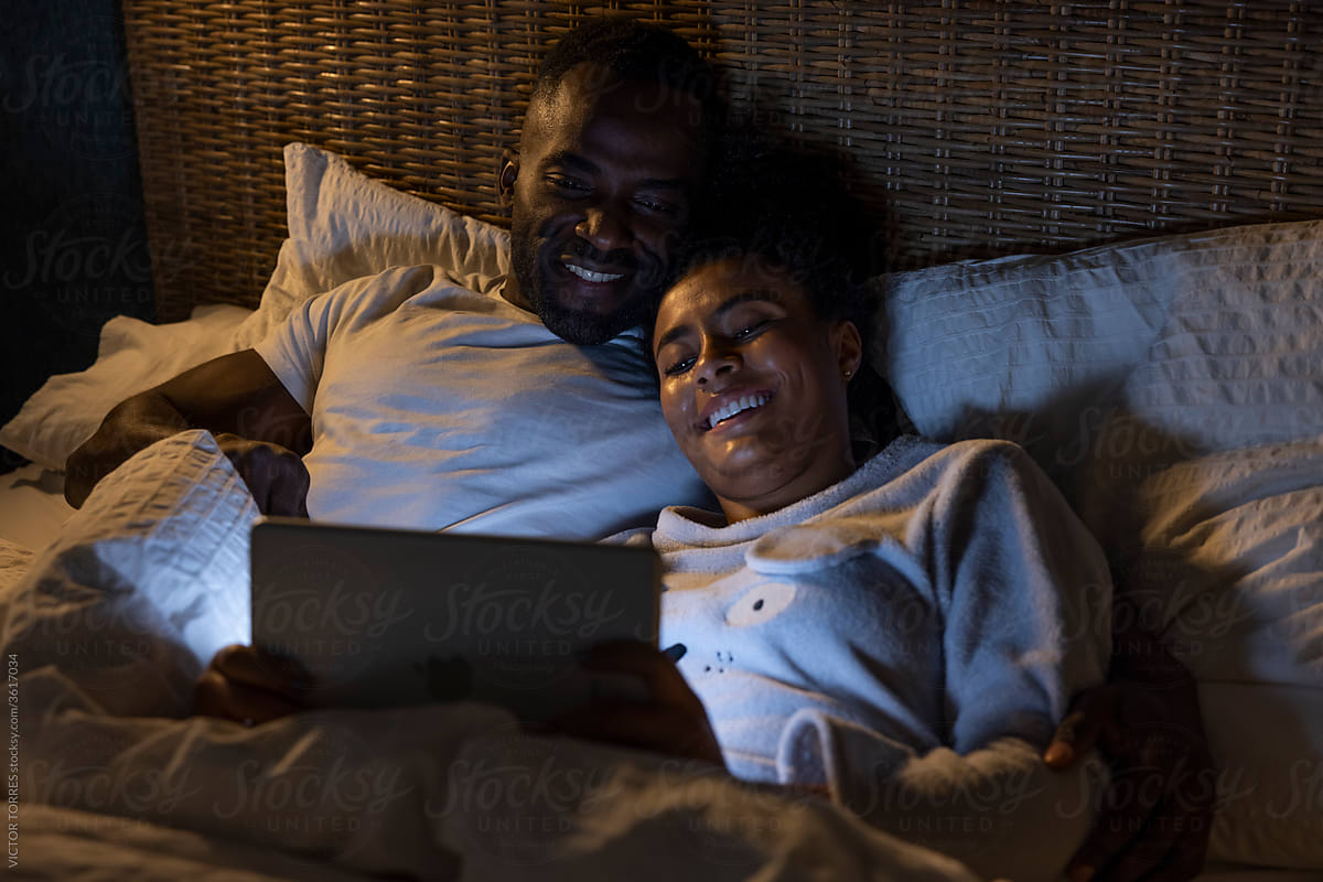 Black couple watching movie on tablet in bed
