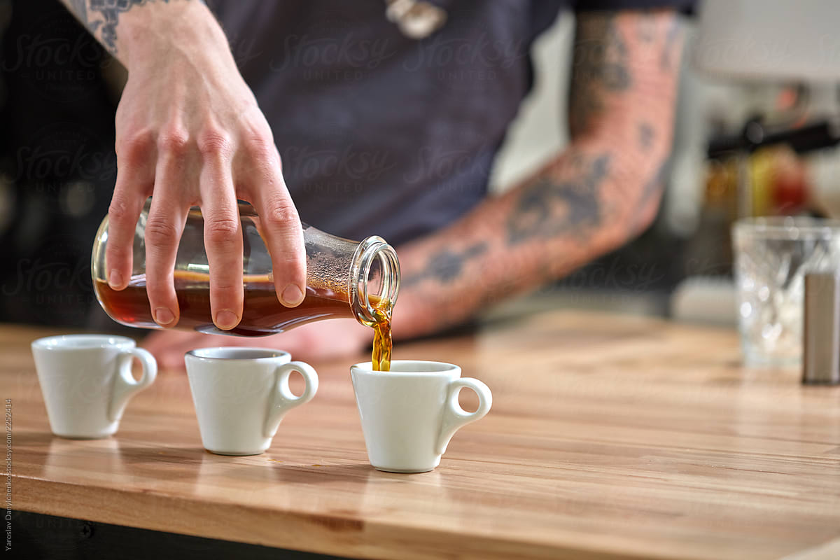 Barista pours coffee from glass bottle to three cups