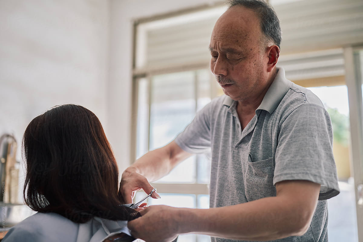 Older Asian Hairstylist Cuts A Customer\'s Hair At His Salon.