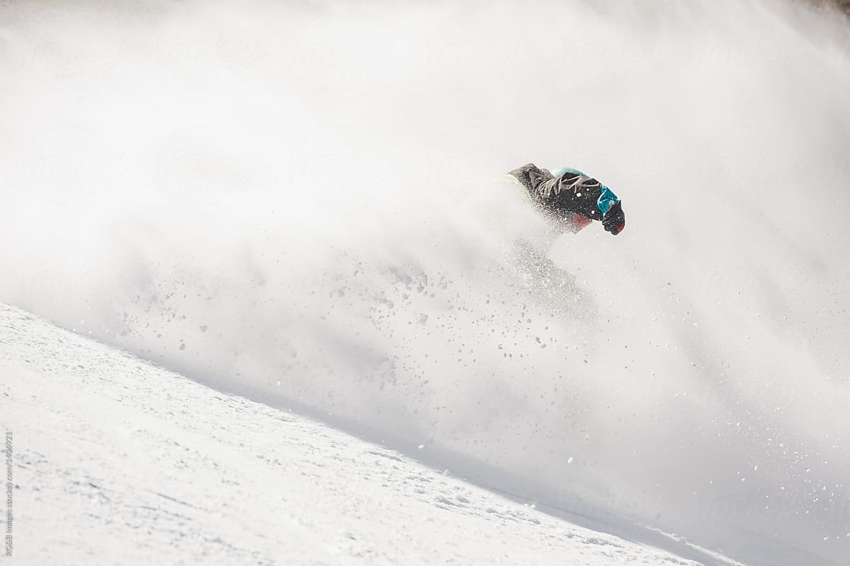 Anonymous man snowboarding through snow avalanche