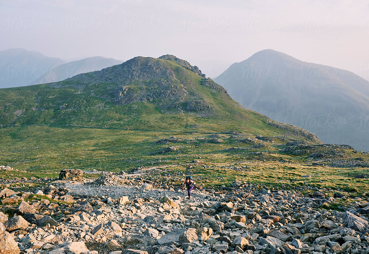 Female walker at sunrise climbing up to Scafell Pike with Lingmell and Great Gable behind.