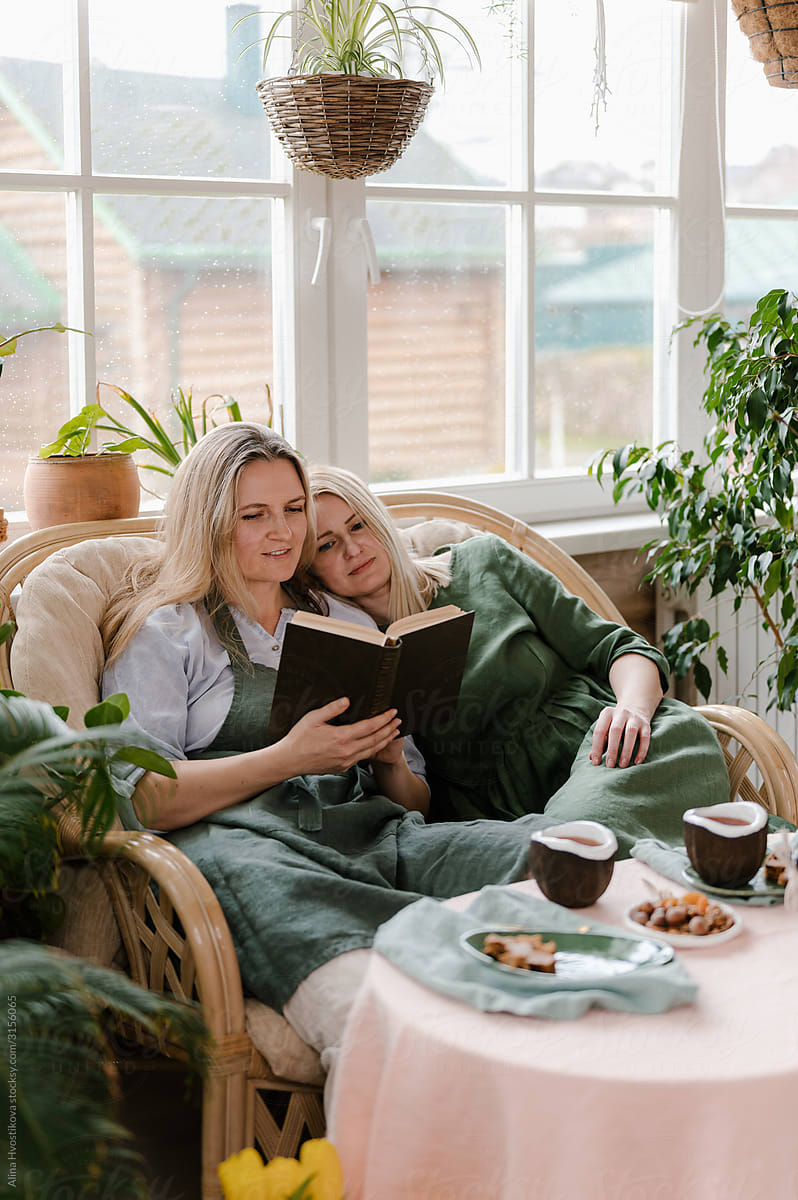 Happy women resting on sofa with book