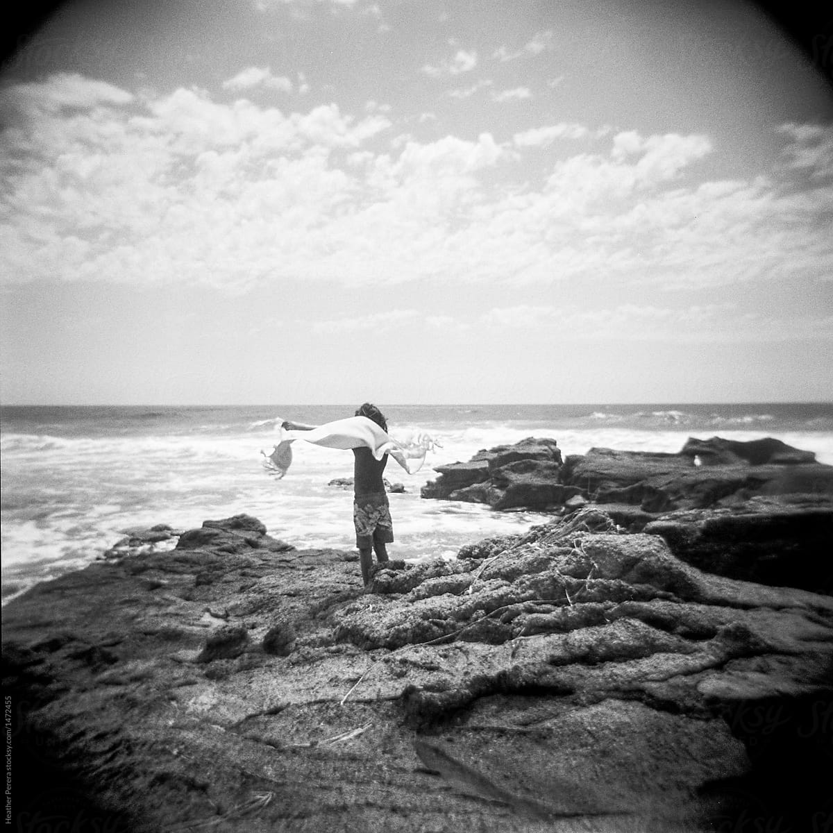 boy with towel in the wind on rocks near ocean