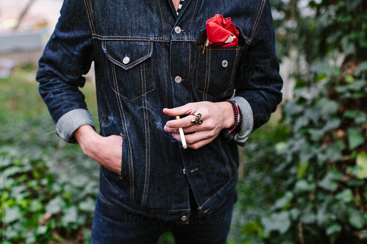 A man in a denim jacket holding a cigarette