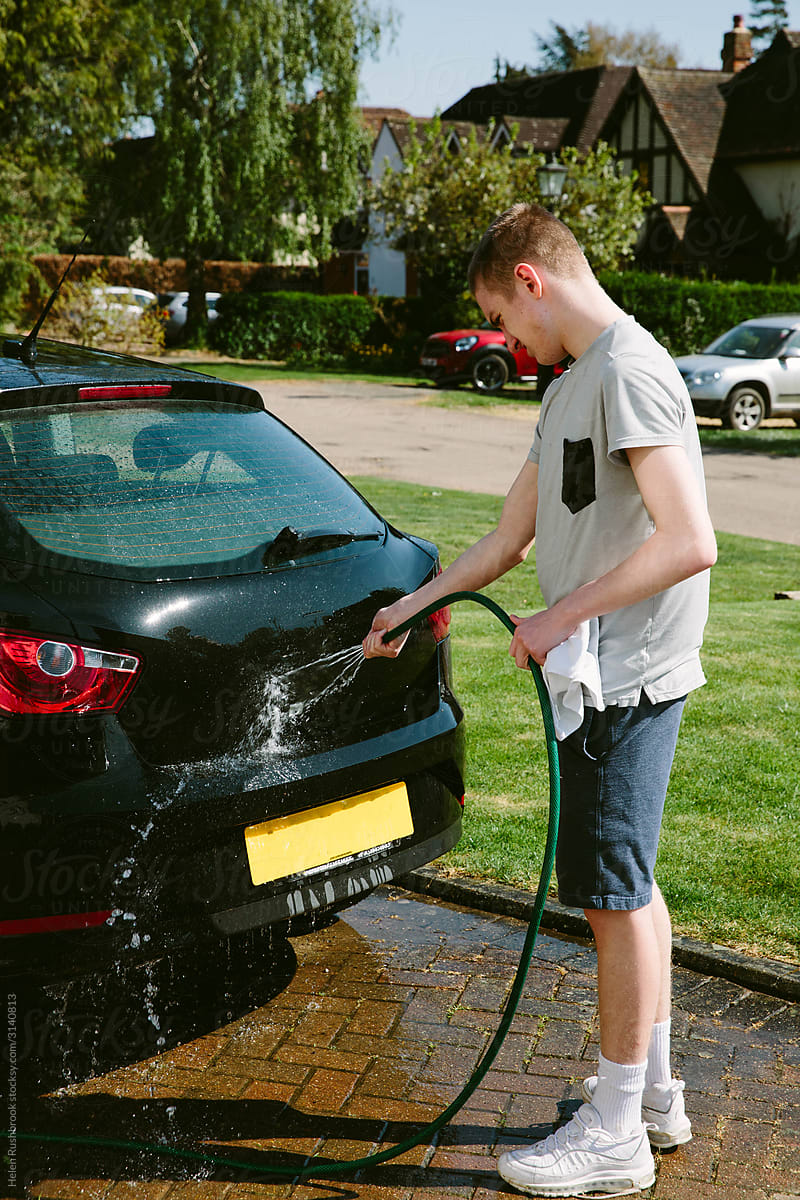 Teenage boy washing his first car on a suburban street