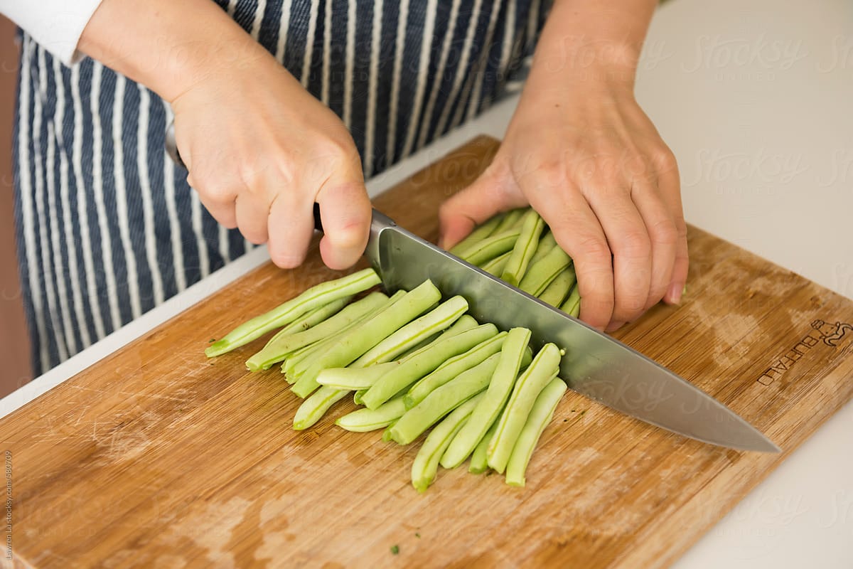 Female hands cutting green beans in kitchen background.