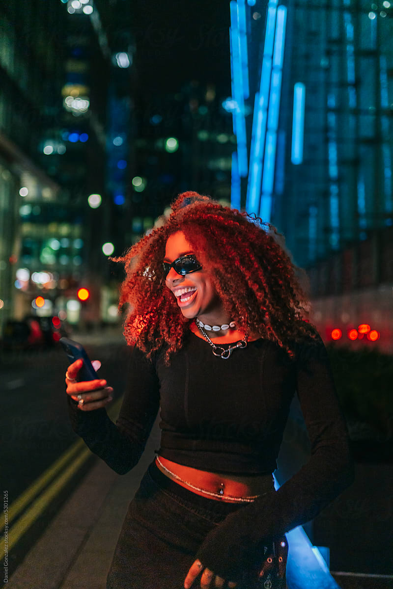 A happy afro girl looks at her cell phone in the night city