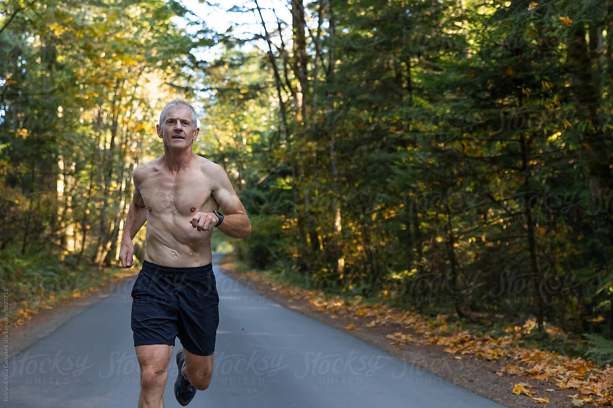 Fit man running hard on road in autumn or fall.