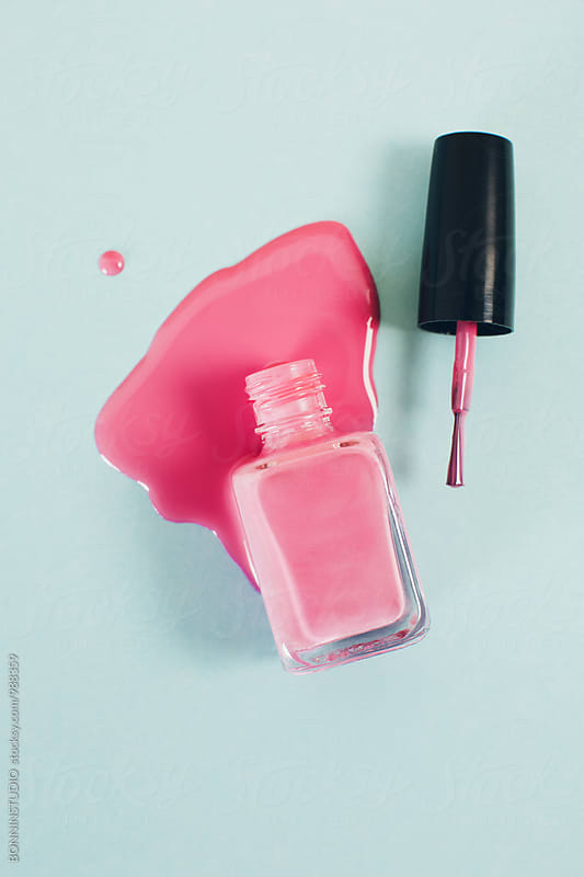 Pink nail polish bottle in puddle of nail polish liquid.