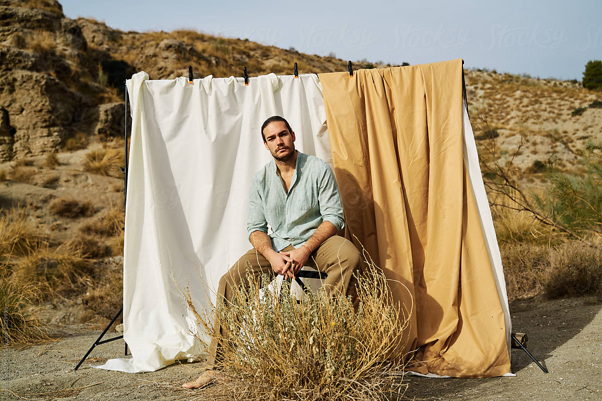 Man sitting outdoors in front of hanging cloths.