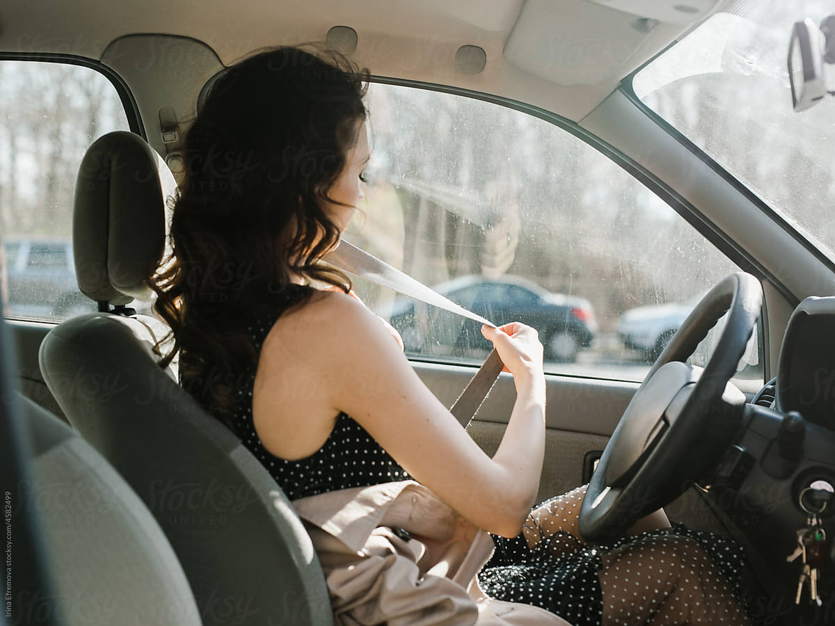 Beautiful woman putting seatbelt on before starting a car