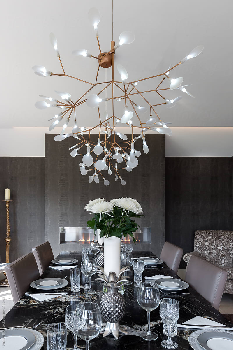 Black granite dining table set for dinner with large ceiling lamp above.