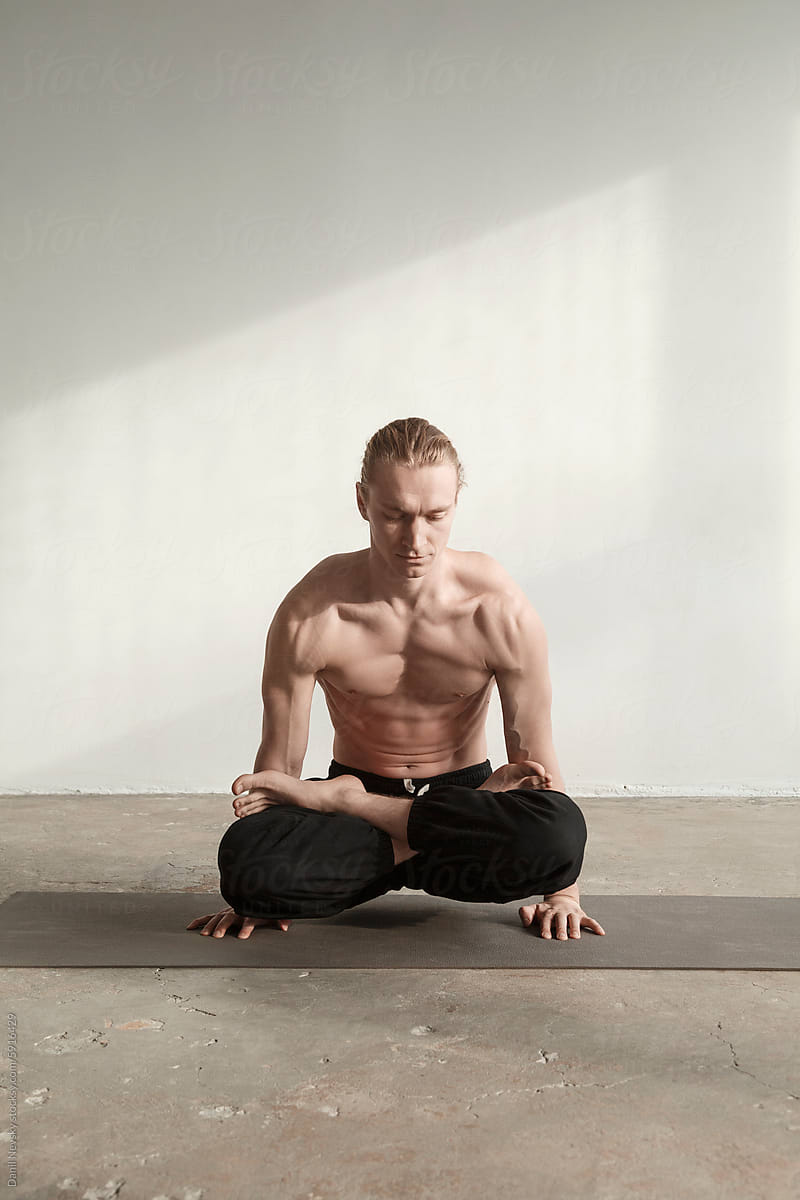 Shirtless fit sportsman performing scale pose in yoga studio