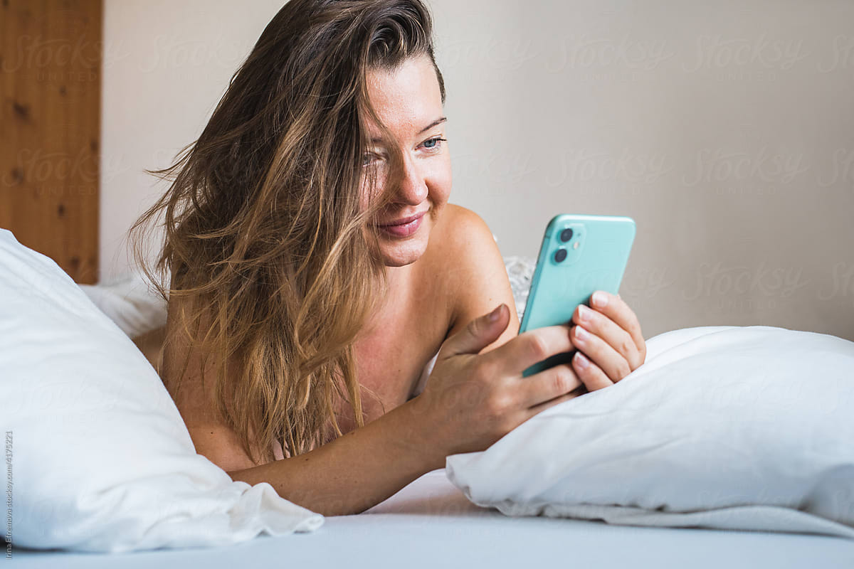 Woman in bed on the phone texting happy