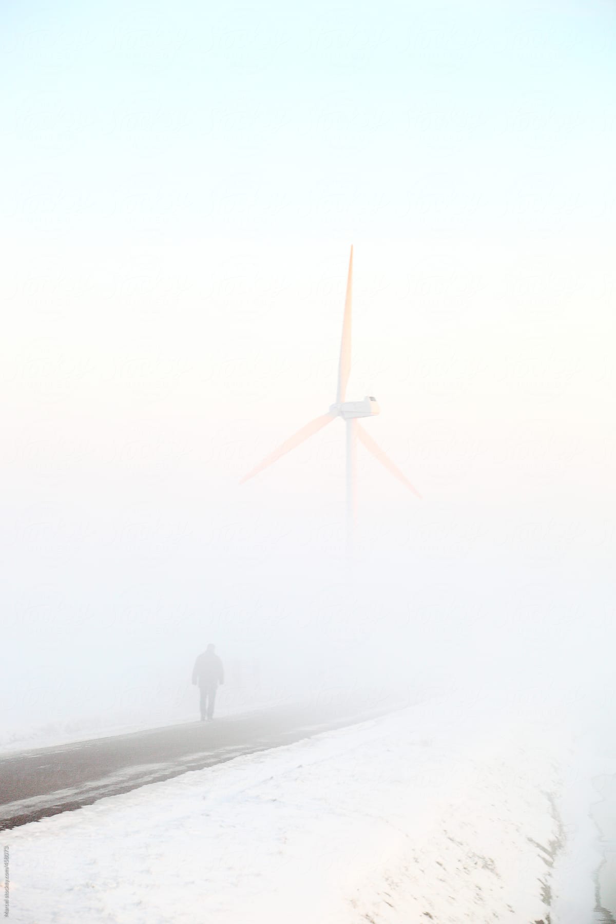 Walking man and windmill in dense fog in the winter