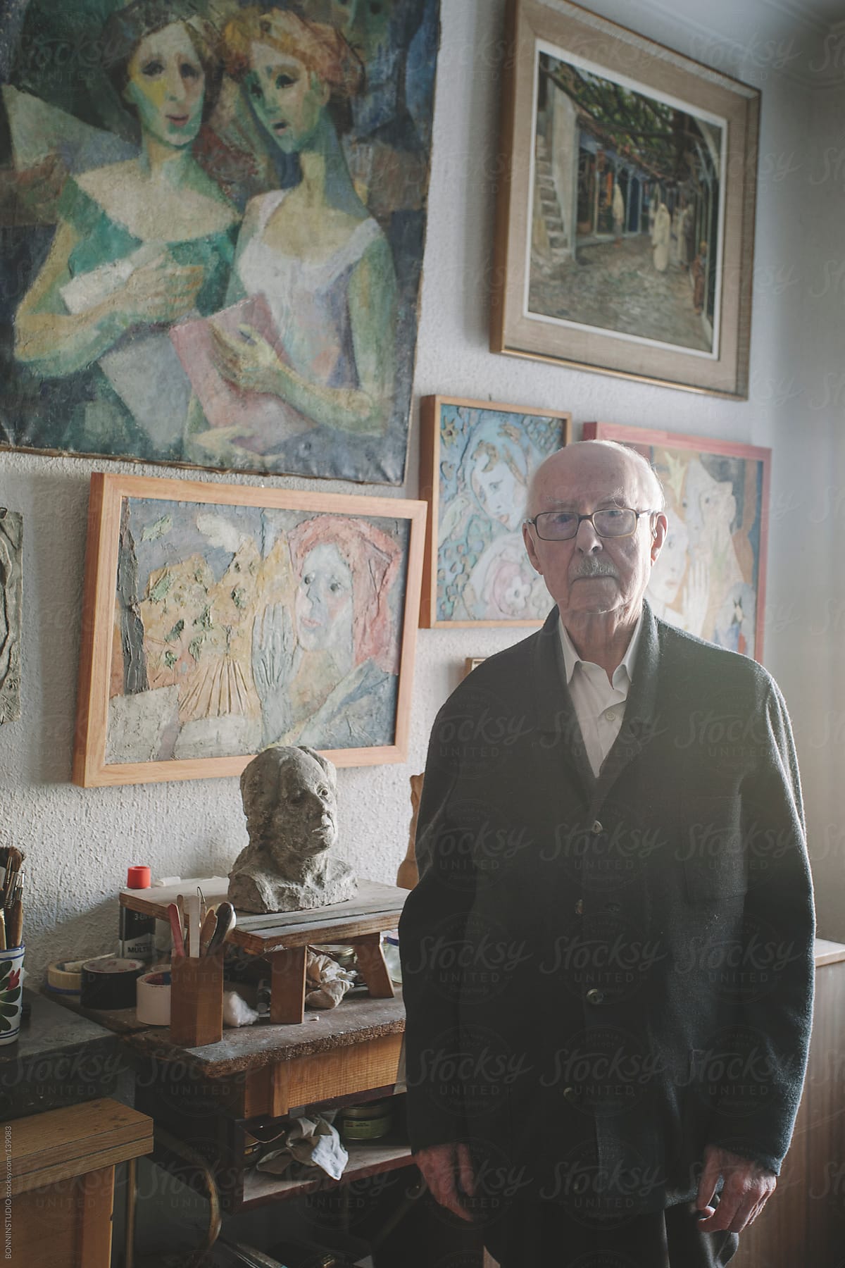 Portrait of old man standing in his studio of painting and sculpture.