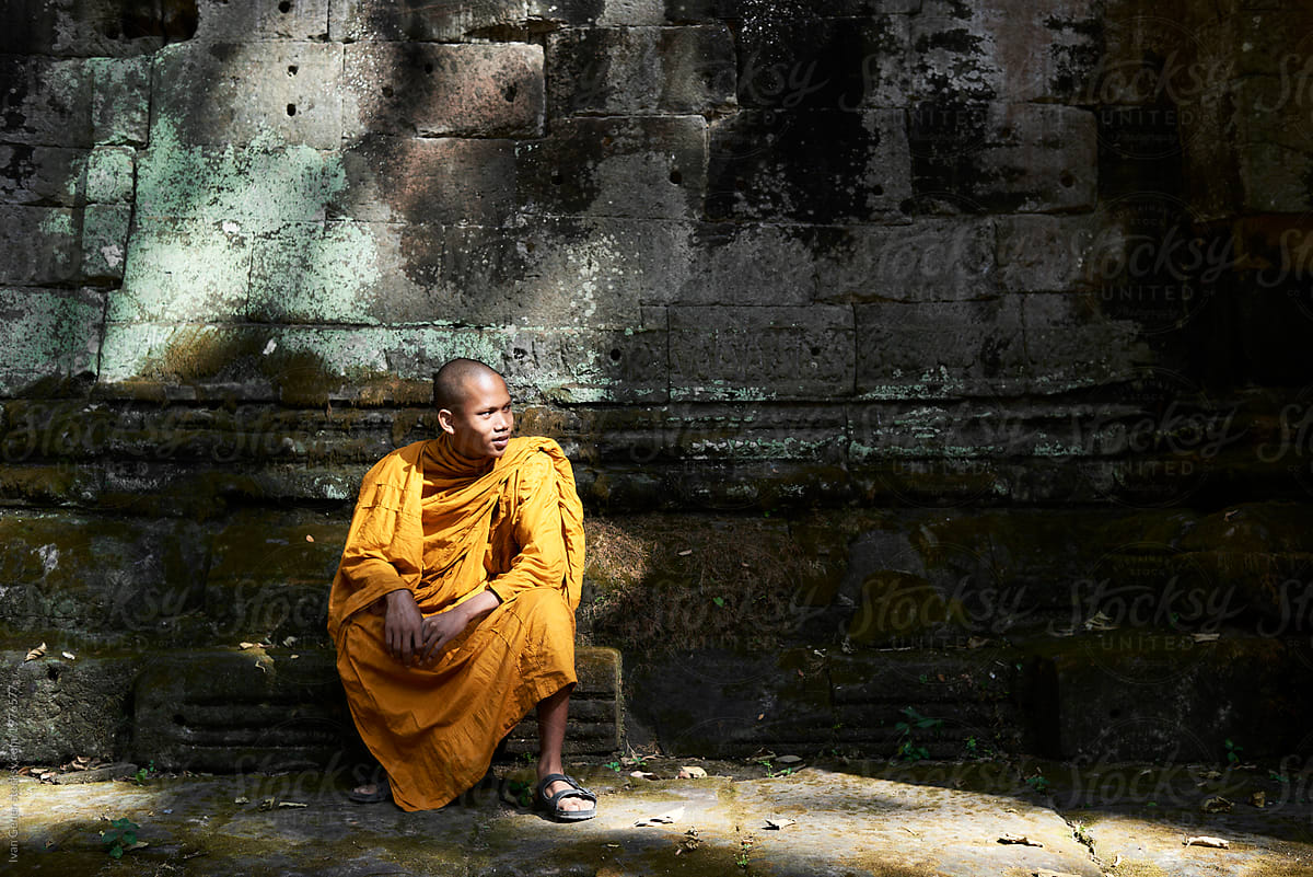 Monk in orange clothes sitting at stone