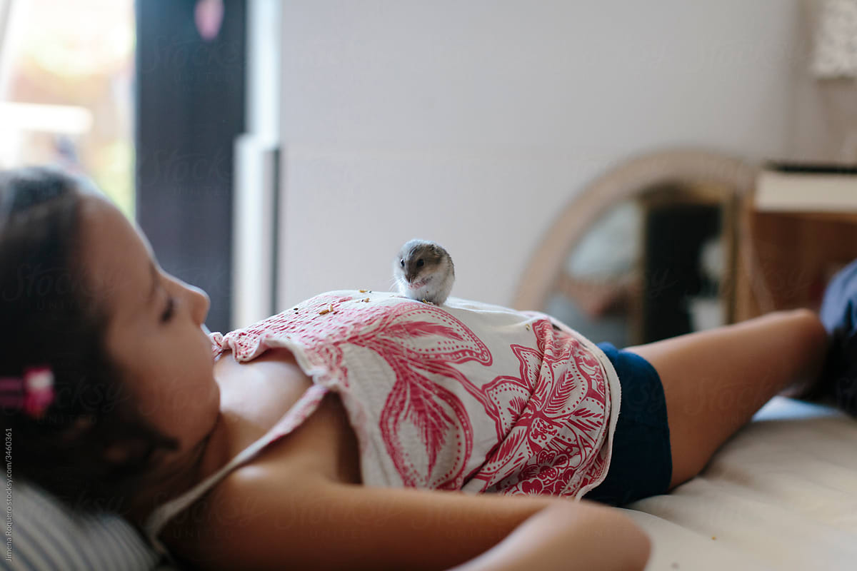 Kid laying on bed with hamster on her belly