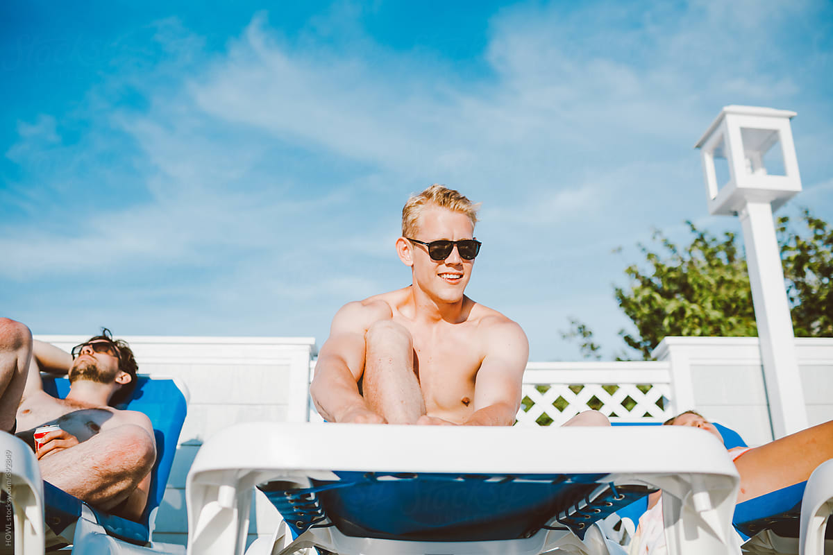 Strong young blonde man sits on lounge chair by pool