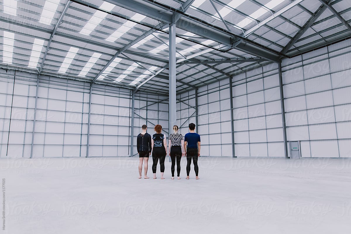 Four people standing with their backs turned away in a large empty warehouse space