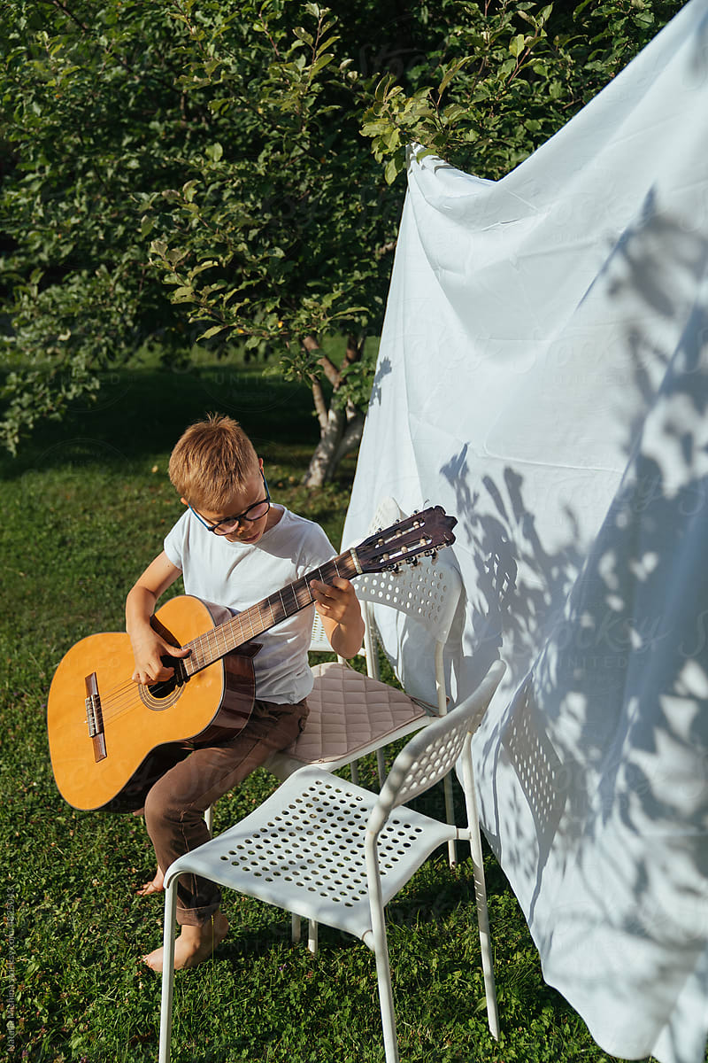A boy is playing guitar in the garden.