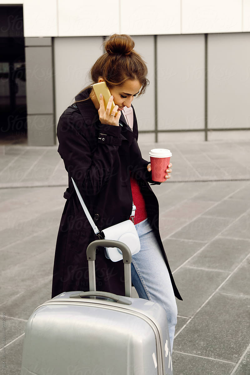 Smiling traveler with cup speaking on phone