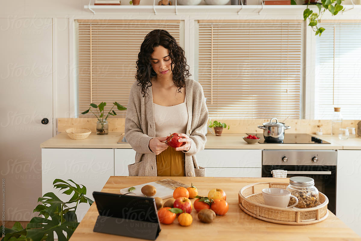 Young woman peeling apple in kitchen