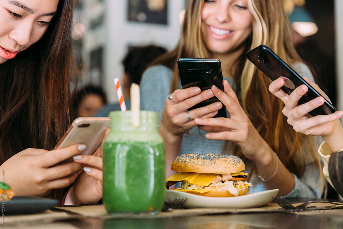 Cropped young women using smartphone and laughing in cafe