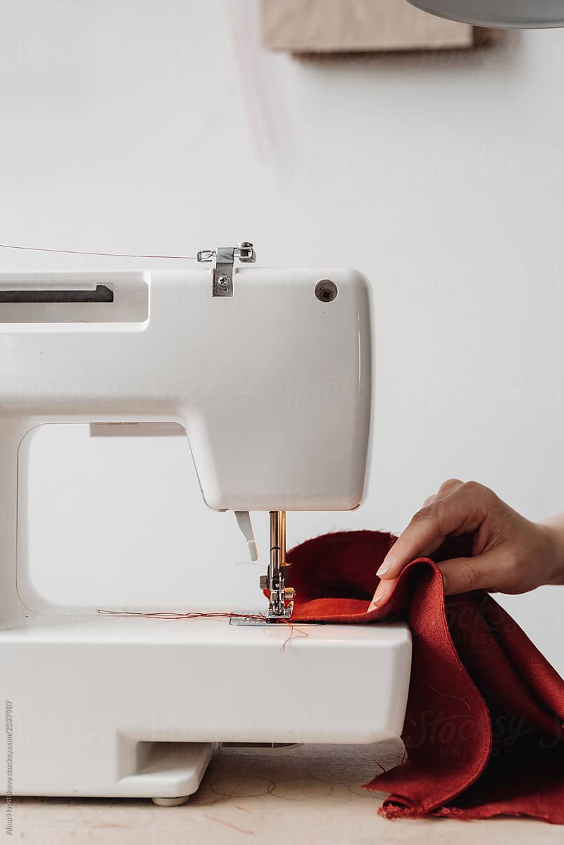 A hand is holding a red cloth on a sewing machine.