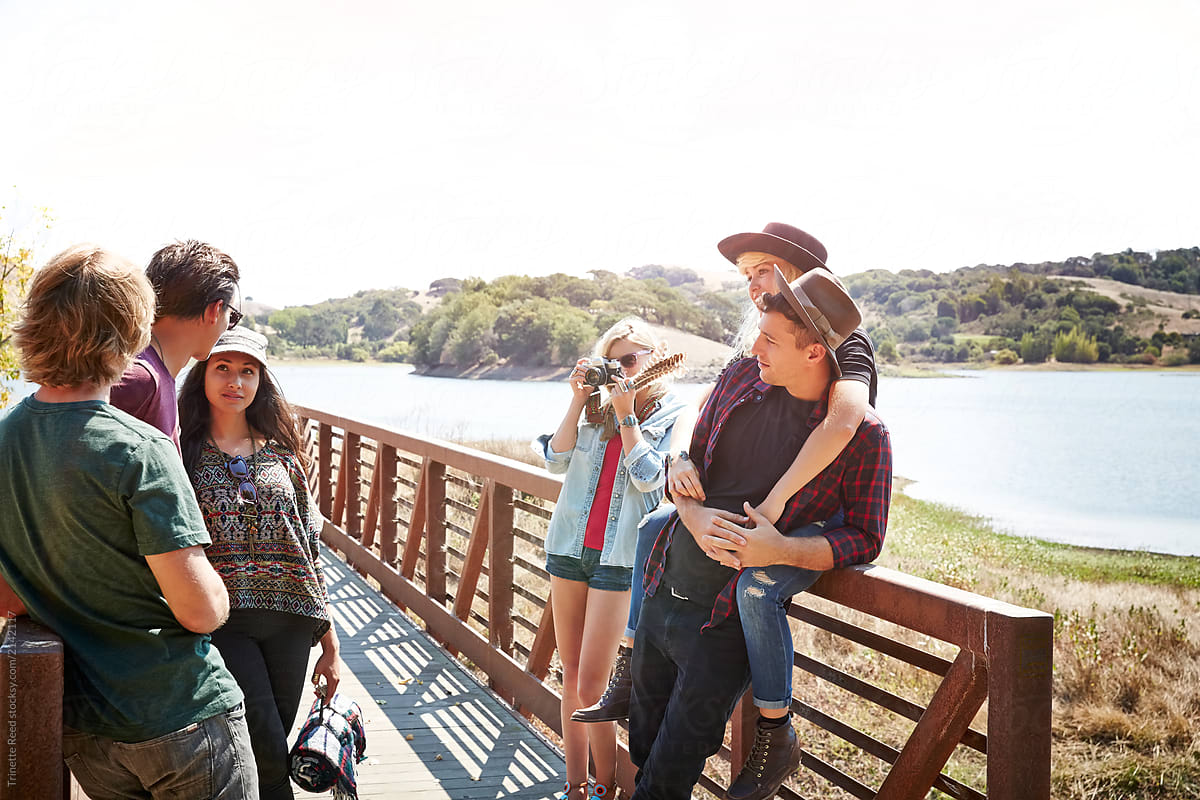 Group of friends hanging out on bridge in nature together while friend takes photo of them