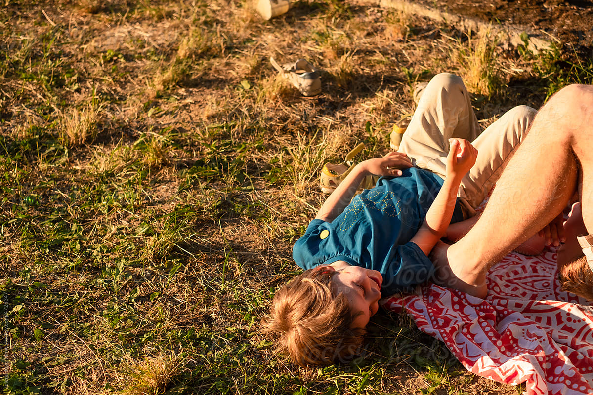 The kid playing outdoors with his dad, laying on a rug in a park