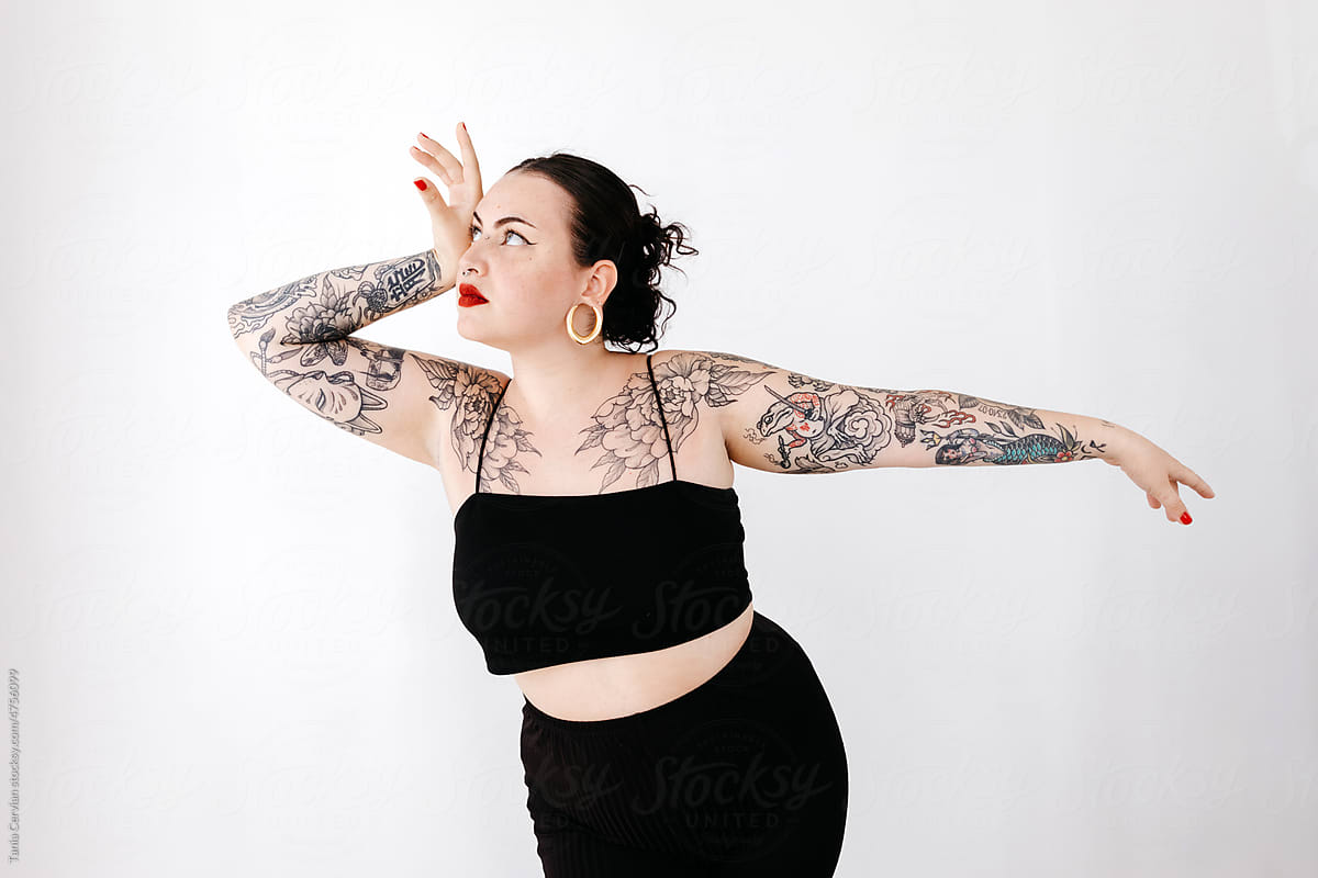 Tattooed curvy woman touching face in studio