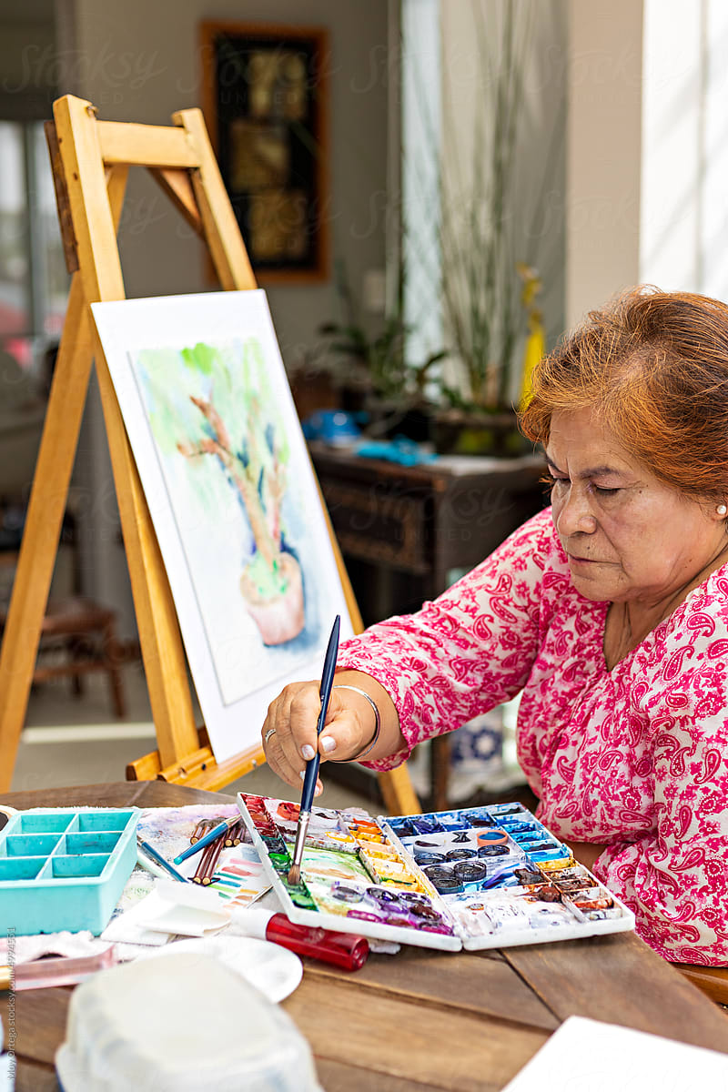 Old woman having good time painting bonsai tree on easel canvas