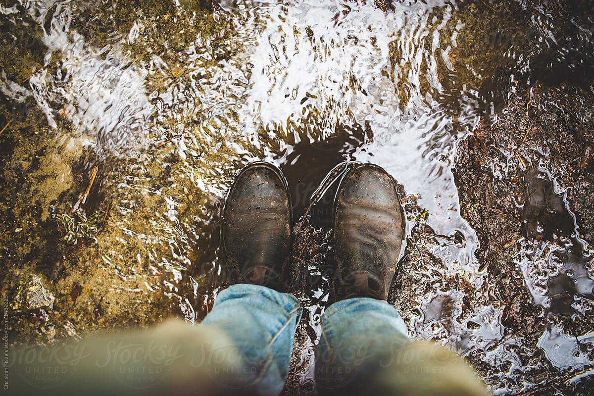 POV of legs wearing light denim jeans and dark leather boots standing in the mud