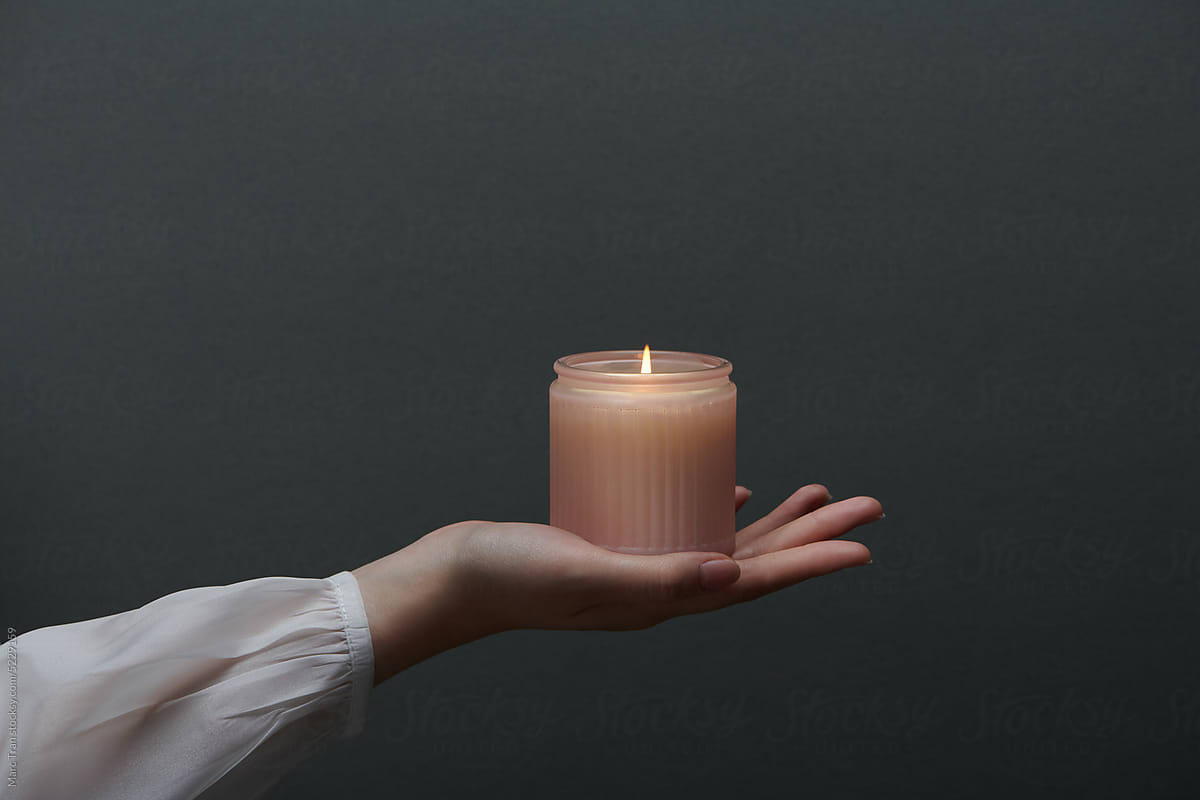 a hand holding a natural soy wax candle with pink glass bottle