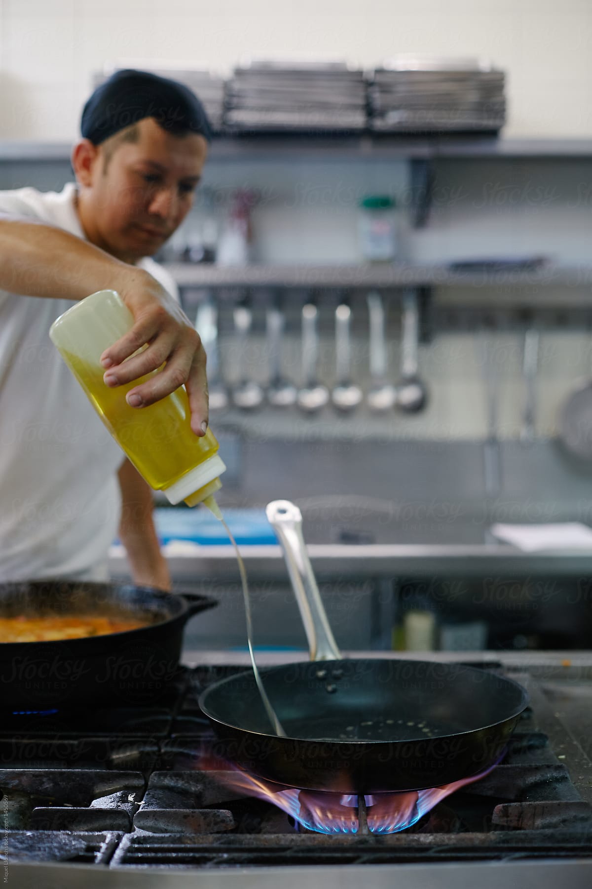 Professional cook adding oil to frying pan on the burner