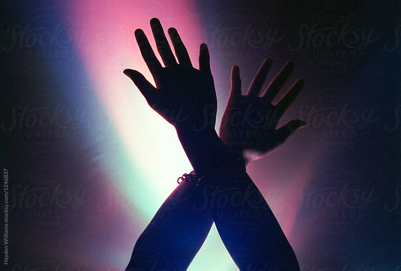 Woman\'s hands in the air in front of bright purple light
