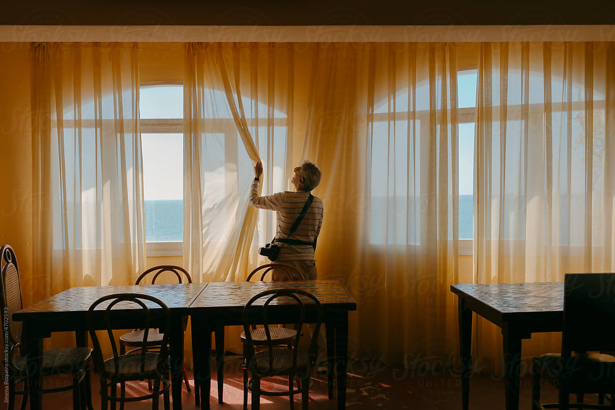 Man in dining room in hotel with warm light opening curtains