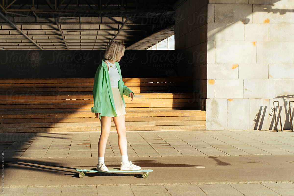 Young woman in trendy outfit standing on longboard