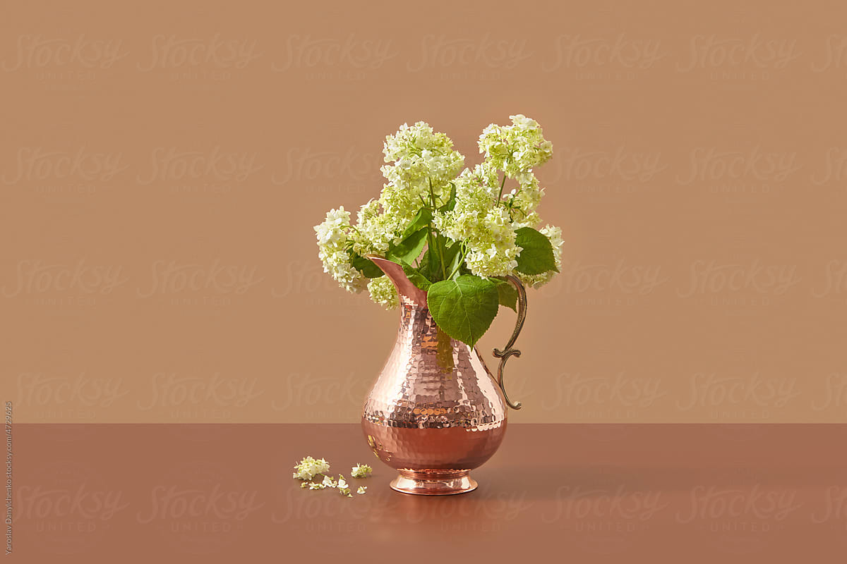 Copper jug with flowers on brown background.