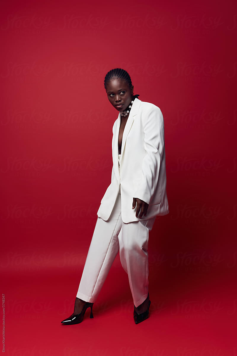 Fashionable black model in white suit posing on red background