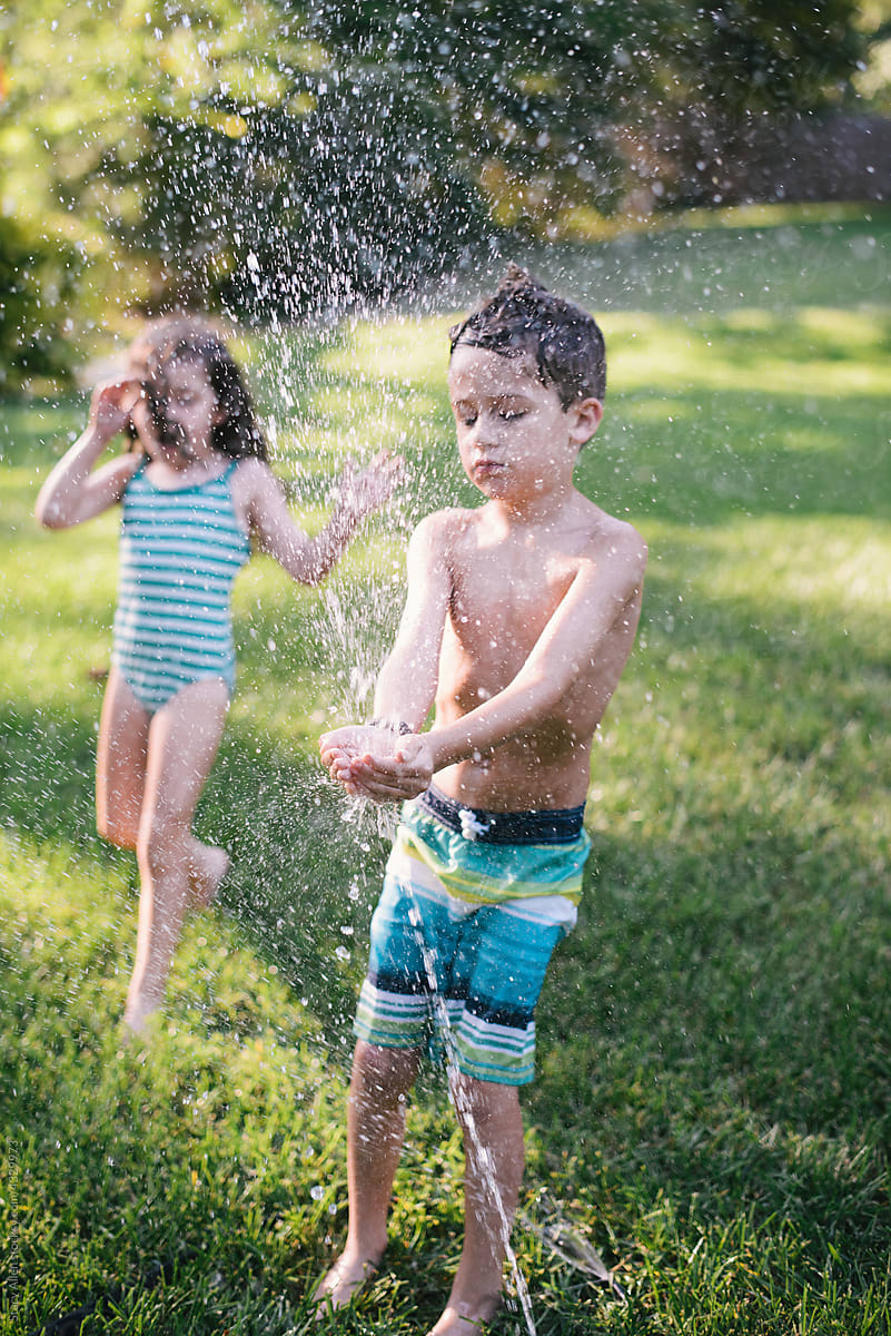 Young siblings playing in a sprinkler