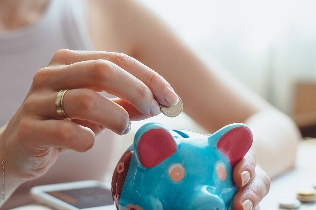 Close up young female hands putting coin in piggy bank.