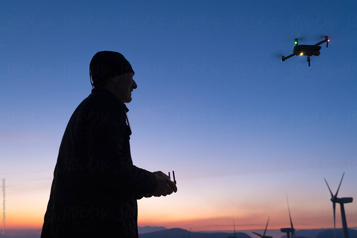 a smilling man is landing his drone in the setting sun